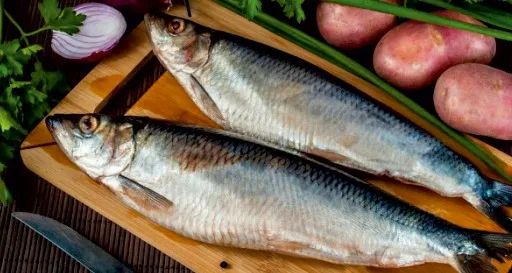 Целая сельдь на деревянной доске с картофелем